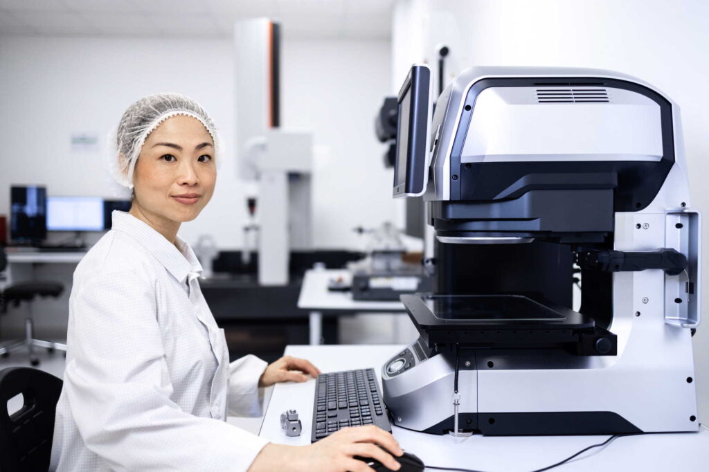 A woman smiling at the camera while working on an analytical machine.