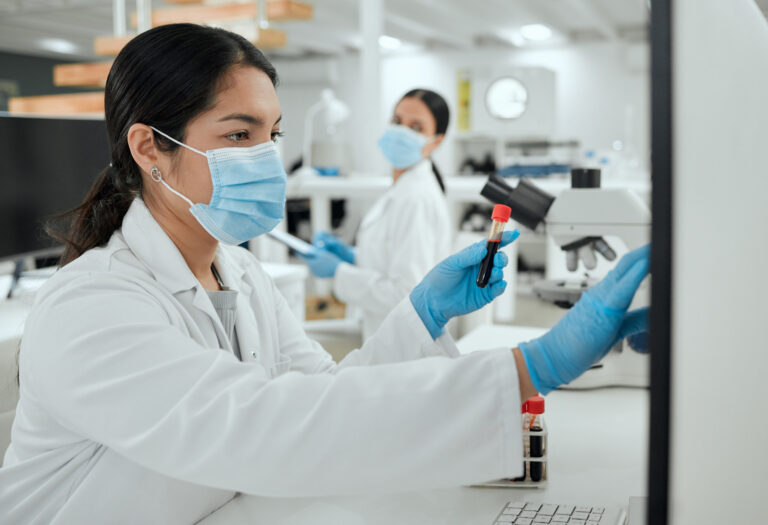 A medical professional reading blood test results while another staff looks from the background.
